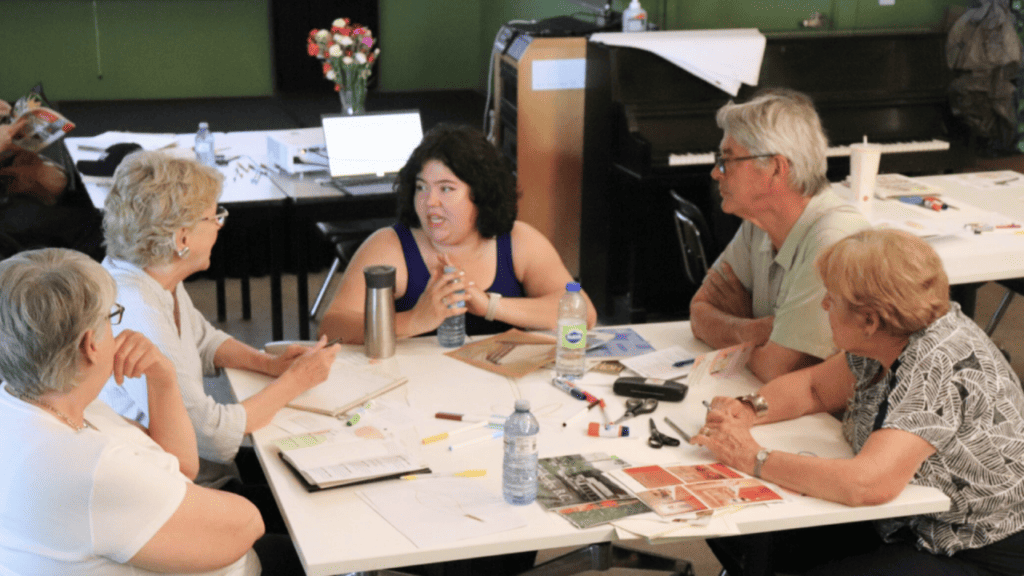 Group of people sit around a table, younger woman in the middle is speaking with four older individuals as part of a workshop on legal literacy